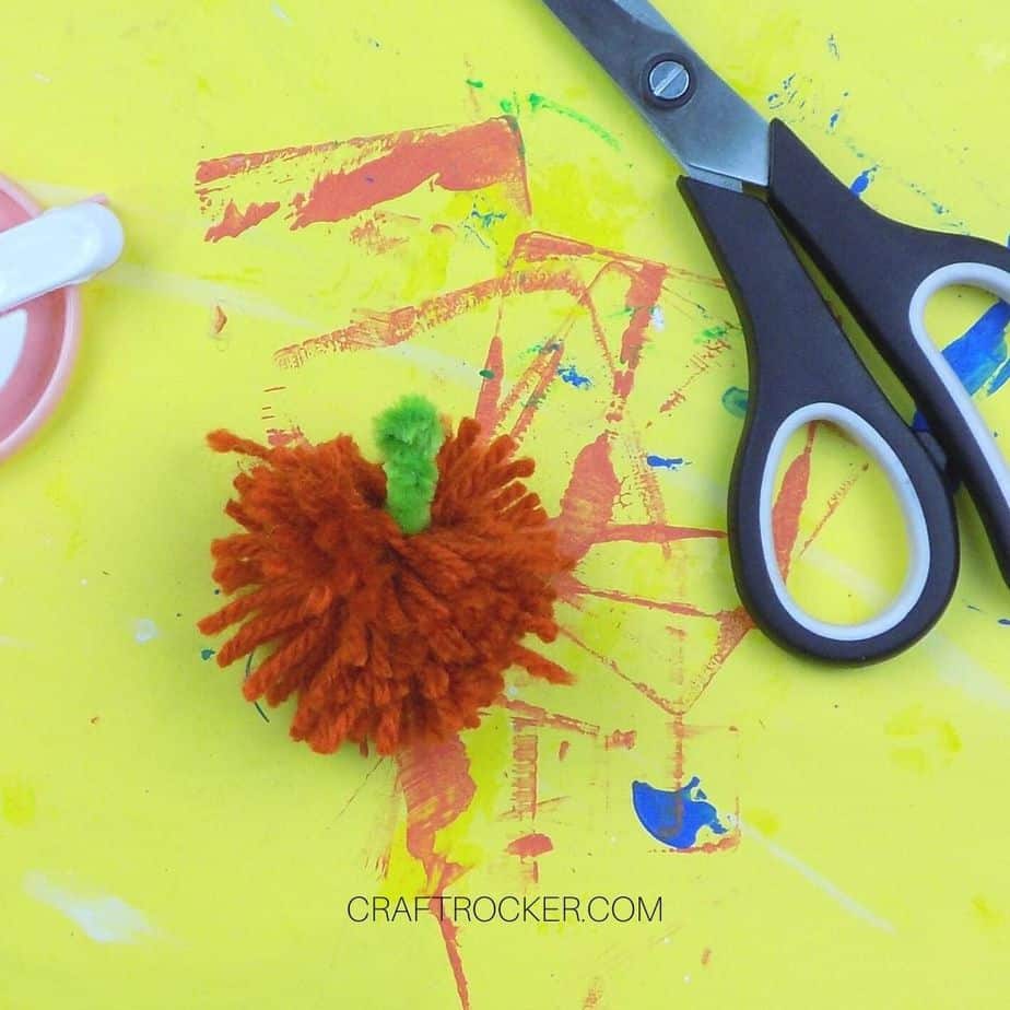 Close Up of Yarn Pumpkin Pom Pom next to Scissors - Craft Rocker