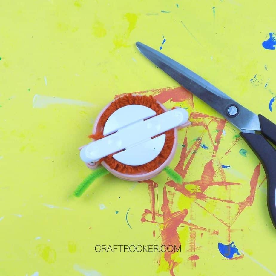 Green Pipe Cleaner Wrapped Around Center of Yarn on Pom Pom Maker - Craft Rocker