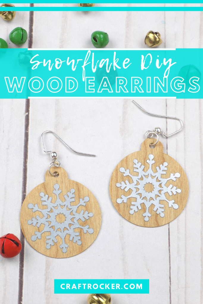 Close Up of Christmas Earrings next to Bells on Wood Background with text overlay - Snowflake DIY Wood Earrings - Craft Rocker