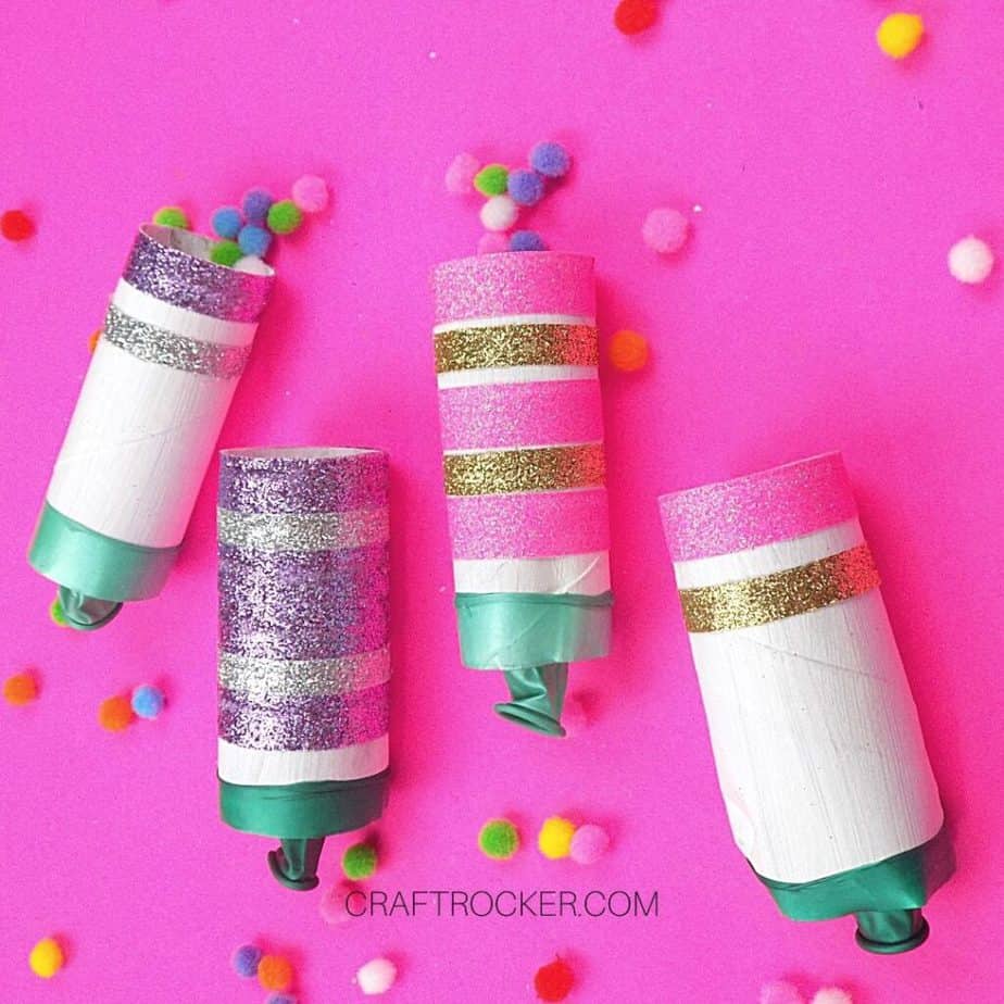 Glittery DIY New Years Poppers on Pink Background next to Pompoms - Craft Rocker