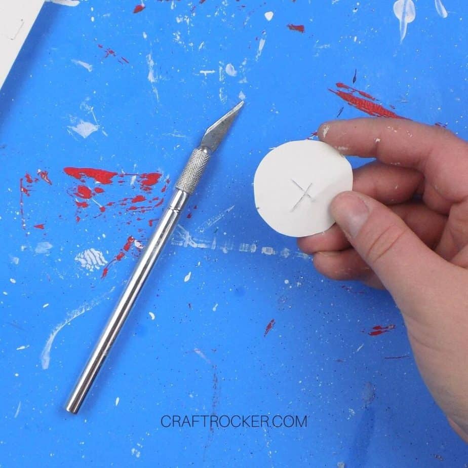 Hand Holding White Circle with x Cut in the Center next to Craft Knife - Craft Rocker