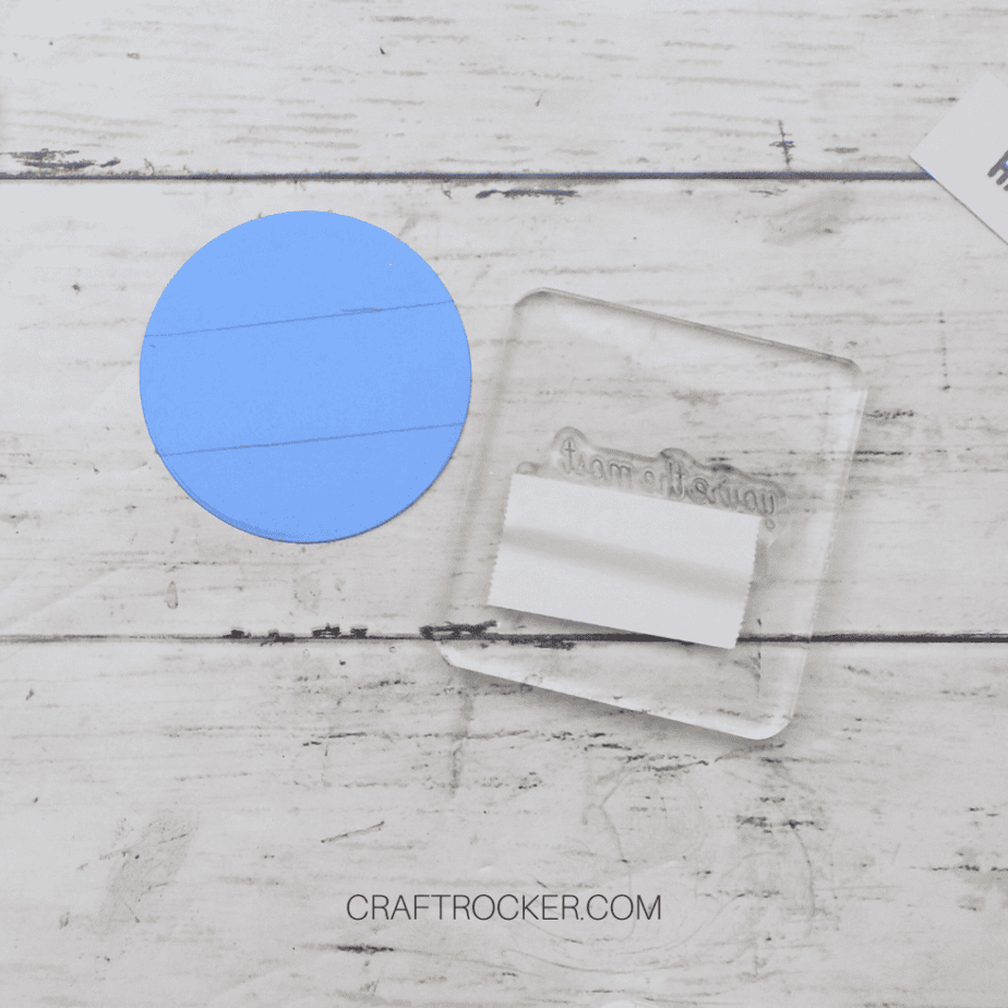 Stamp on Acrylic Block with Tape Over it next to Blue Paper Circle - Craft Rocker